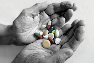 Das Bild zeigt die Hände eines alten Menschen. In den Handflächen liegen verschiedene Tabletten und Pillen.