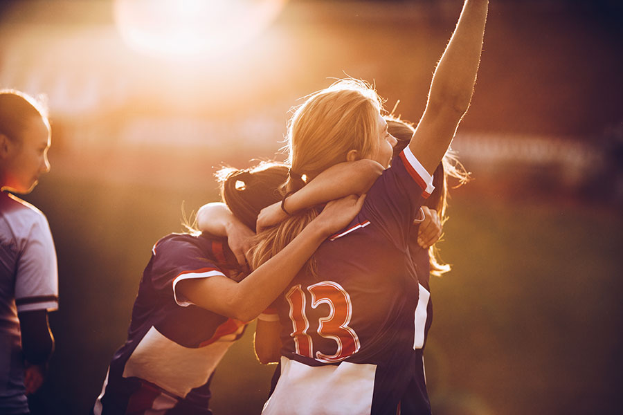 Fußballspielerinnen feiern ihren Erfolg auf einem Fußballplatz bei Sonnenuntergang.