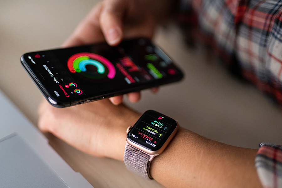 Eine Hand hält Smartphone und gleicht Daten mit Smartwatch an der anderen Hand ab