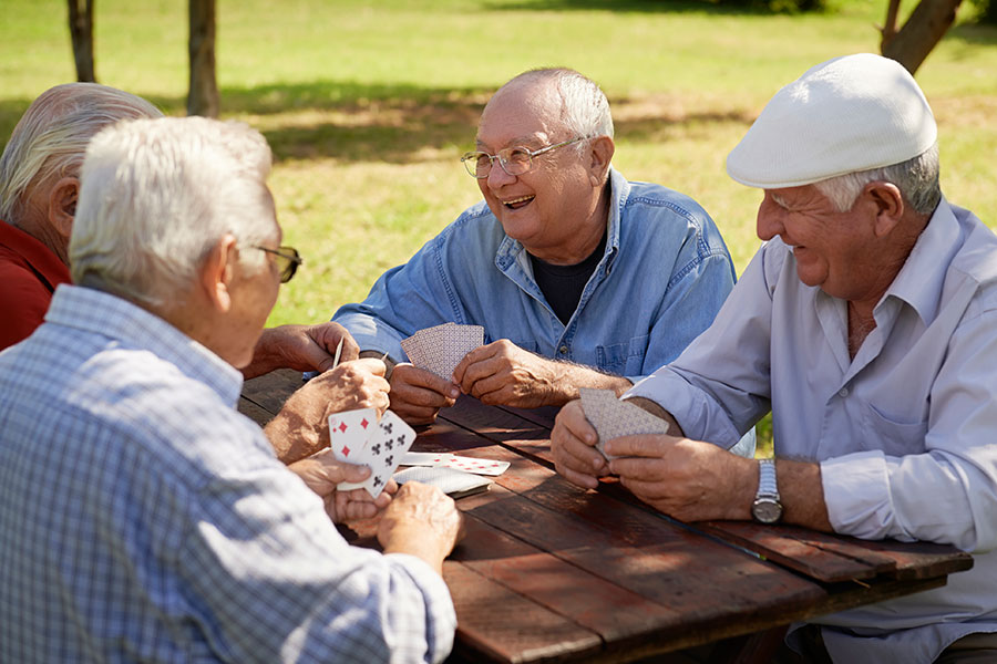 Drei ältere Herren sitzen draußen an einem Holztisch und spielen Karten.