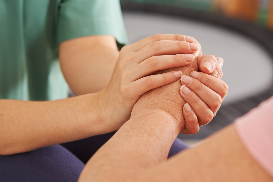 Die Hände einer jungen Pflegenden halten die Hand einer älteren Frau. 