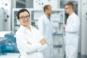 Wissenschaftlerin im Vordergrund des Bildes und Klinikmitarbeitende in einem Labor