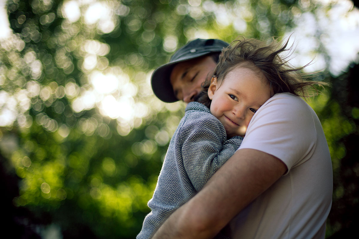 Kind auf dem Arm des Vaters, während Wind mit seinen Haaren spielt.