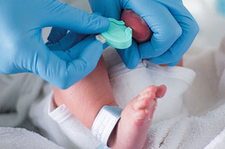 Medizinische Fachkraft nimmt Neugeborenem Blut ab.