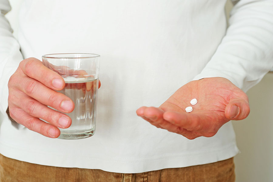 Hände halten ein Glas Wasser und zwei Tabletten.
