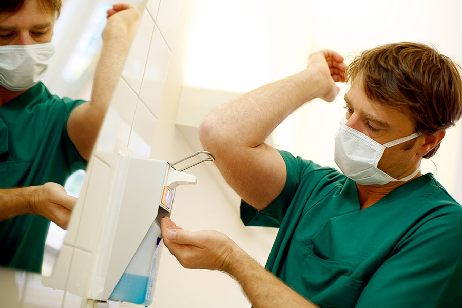 Medizinischer Fachangestellter mit Mund-Nasen-Schutz desinfiziert sich die Hände
