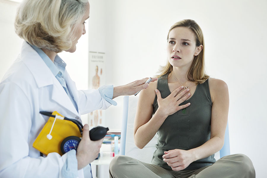 Patientin, die sich die Hand auf den Brustkorb legt, spricht mit einer Ärztin