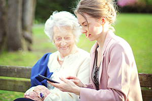 Junge Frau mit älterer Dame auf einer Parkbank sitzend schauen auf ein Handy