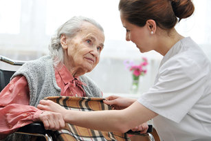 Pflegerin deckt alte Dame im Rollstuhl mit einer Decke zu.