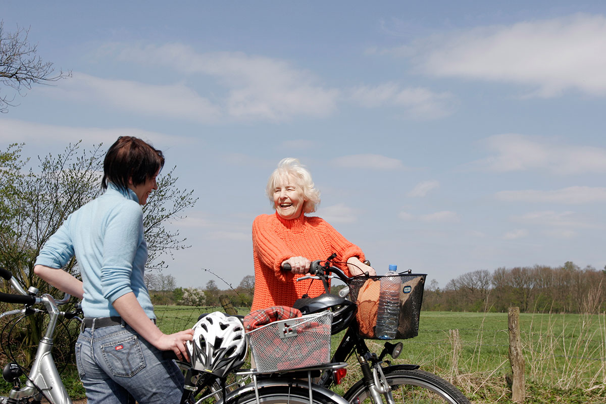 Eine ältere und eien jüngere Frau begegnen sich mit dem Fahrrad und unterhalten sich.