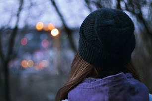 Eine junge Frau mit Mütze schaut wie durch ein Fenster in die graue Landschaft.
