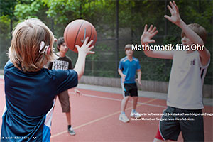 Kinder beim Ballspielen auf einem Sportplatz. Ein Junge trägt ein Hörgerät.