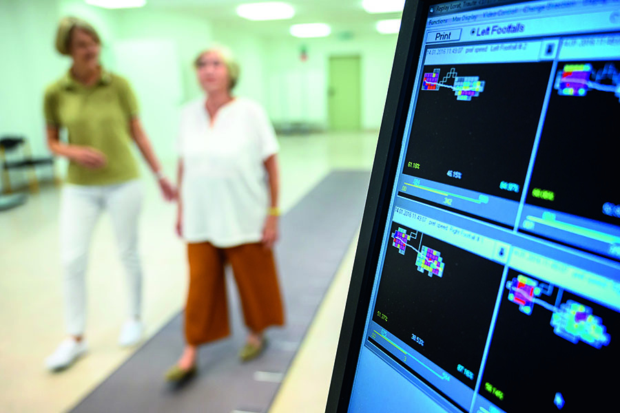 Computer-Bildschirm zeichnet Gangmuster auf, im Hintergrund Patientin mit Therapeutin 
