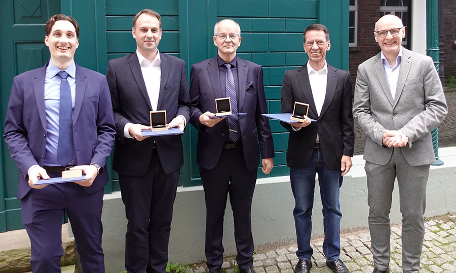 Fünf stehende Herren, davon vier mit Medaillen und Urkunden in der Hand