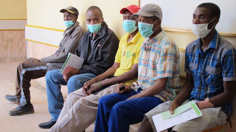 Fünf Männer mit Mundschutz sitzen in einem Warteraum.