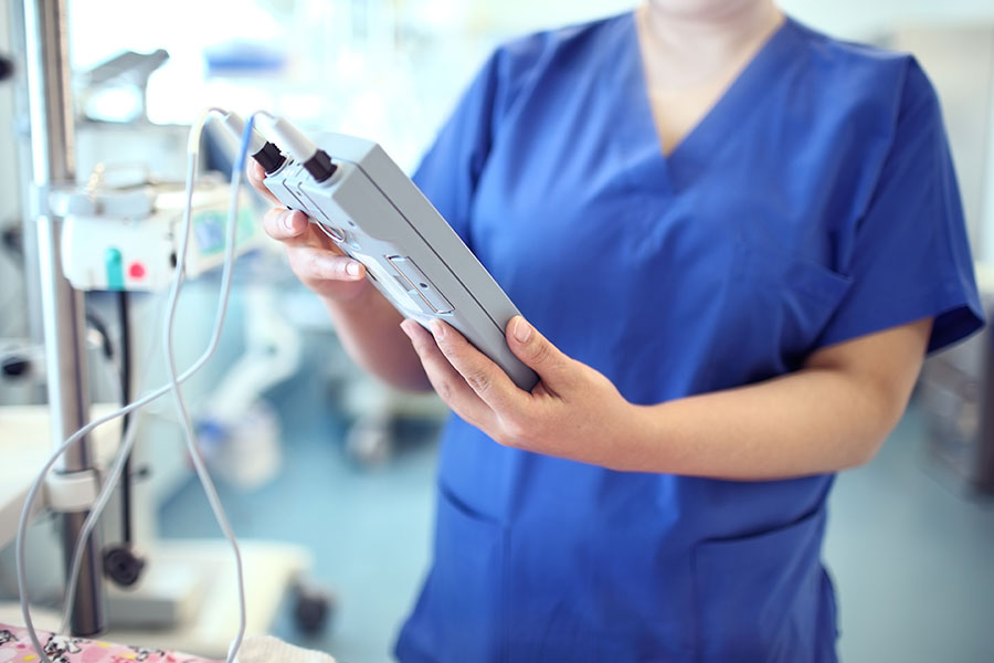 Frau im blauen OP-Kittel schaut auf ein elektronisches medizinisches Gerät