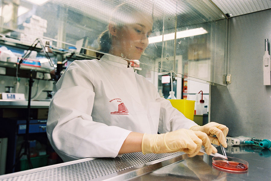 Junge Wissenschaftlerin arbeitet mit Kittel und Handschuhen an einer sterilen Laborbank.