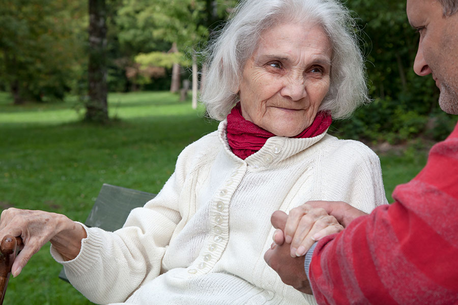 Eine alte Frau und ein jüngerer Mann sitzen in einem Park auf einer Bank. Der Mann hält die Hand der Frau.