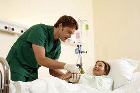 Ein Pfleger beugt sich über das Krankenbett einer Patientin