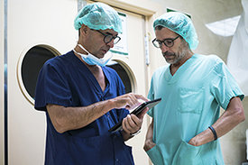 Zwei Chirurgen stehen auf Krankenhausflur und benutzen ein Tablett