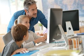 Zwei Kinder betrachten mit Unterstützung eines Mannes einen Computerbildschirm. 
