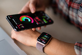 Eine Hand hält Smartphone und gleicht Daten mit Smartwatch an der anderen Hand ab