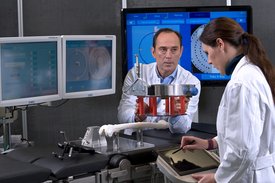 Ein Mann und eine Frau in weißen Kitteln diskutieren vor Bildschirmen in einem Labor.