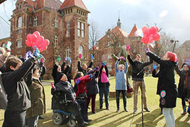 Eine Gruppe von Menschen, die bunte Handschuhe tragen, lassen rote Luftballons steigen. 