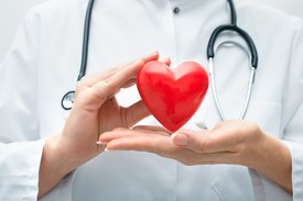 Ärztin hält rotes Kunststoff-Herz zwischen ihren Händen 