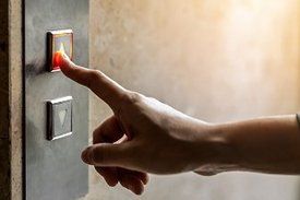 Eine Person drückt mit dem Zeigefinger auf einen Knopf an einem Aufzug