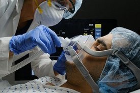 Ärztin überprüft Covid-19-infizierten Patienten, während er an ein Beatmungsgerät angeschlossen ist 