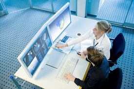 Ärztin und Arzt sitzen vor Monitoren; gemeinsam analysieren sie mithilfe eines Computerprogramms medizinische Bilder.