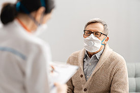 Patient mit Mundschutz im Gespräch mit Ärztin