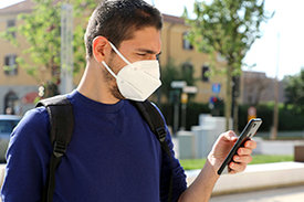 Junger Mann mit FFP2-Maske schaut auf Smartphone