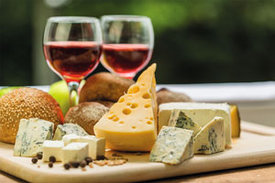 Ein Holztablett mit verschiedenen Käsestücken, Brötchen und zwei Gläsern Rotwein