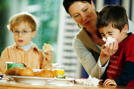 Mutter putzt Kind am Frühstückstisch die Nase.