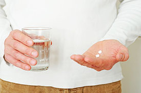 Hände halten ein Glas Wasser und zwei Tabletten.