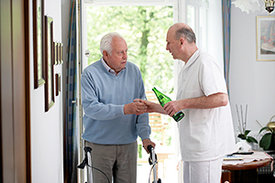 Pfleger in Senioreneinrichtung reicht älterem Herrn ein Glas mit Wasser.