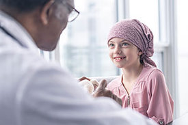 Arzt spricht in Krankenzimmer zu Kind mit rosafarbenem Kopftuch.