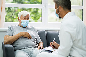 Älterer Patient mit Mundschutz im Gespräch mit Arzt