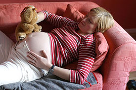 Schwangere Frau auf roter Couch mit Teddy