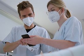 Arzt und Ärztin schauen im Krankenhaus auf ein Smartphone
