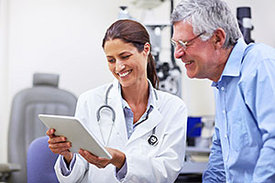 Junge Ärztin und Patient schauen auf ein Tablet in einem Behandlungszimmer.