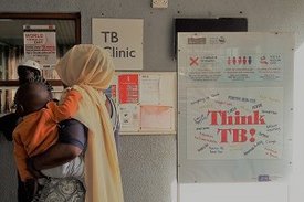 Eine Frau mit einem Kind auf dem Arm steht vor einer Tuberkulose-Klinik in Gambia, Westafrika