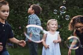 Vier Kinder auf einer Wiese pusten Seifenblasen